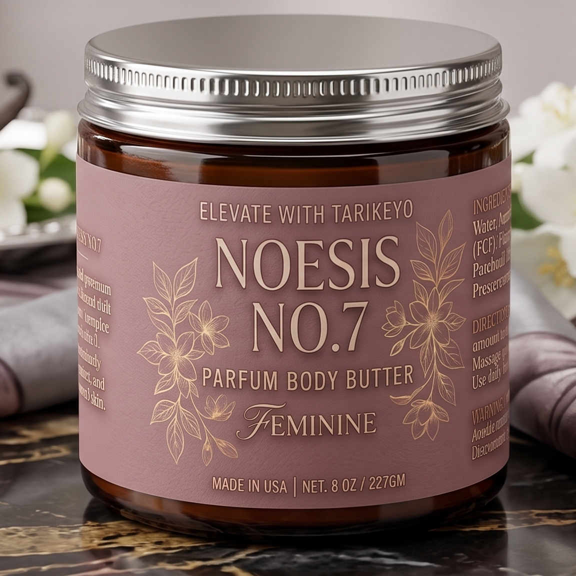 A jar of Elevate With Tarikeyo Noesis No.7 Parfum Body Butter, featuring a dusty rose label with gold lettering and botanical illustrations, set on a dark marble surface with blurred white flowers in the background.